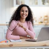 remote-entrepreneurship-happy-millennial-woman-sitting-at-table-with-laptop-in-kitchen-e1703418489331.jpg